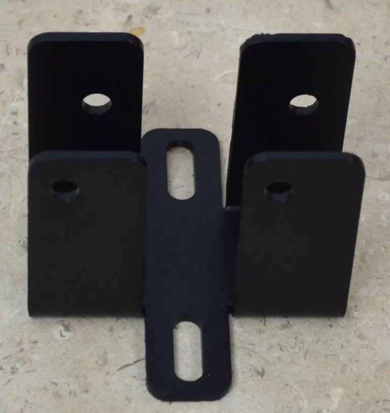 The DIY Rafter Tie Bracket is black, features four upright tabs with holes and two elongated slots on the base, shown on a beige textured surface—perfect for DIY roof bracket projects.