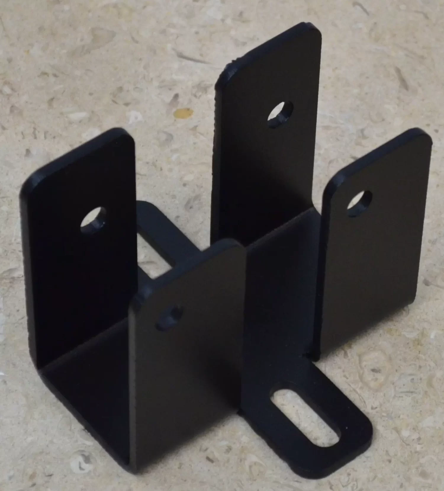 The DIY Rafter Tie Bracket features four vertical sides with circular holes and a horizontal base with an elongated slot, ideal for DIY roof bracket projects. Displayed here on a beige textured surface.