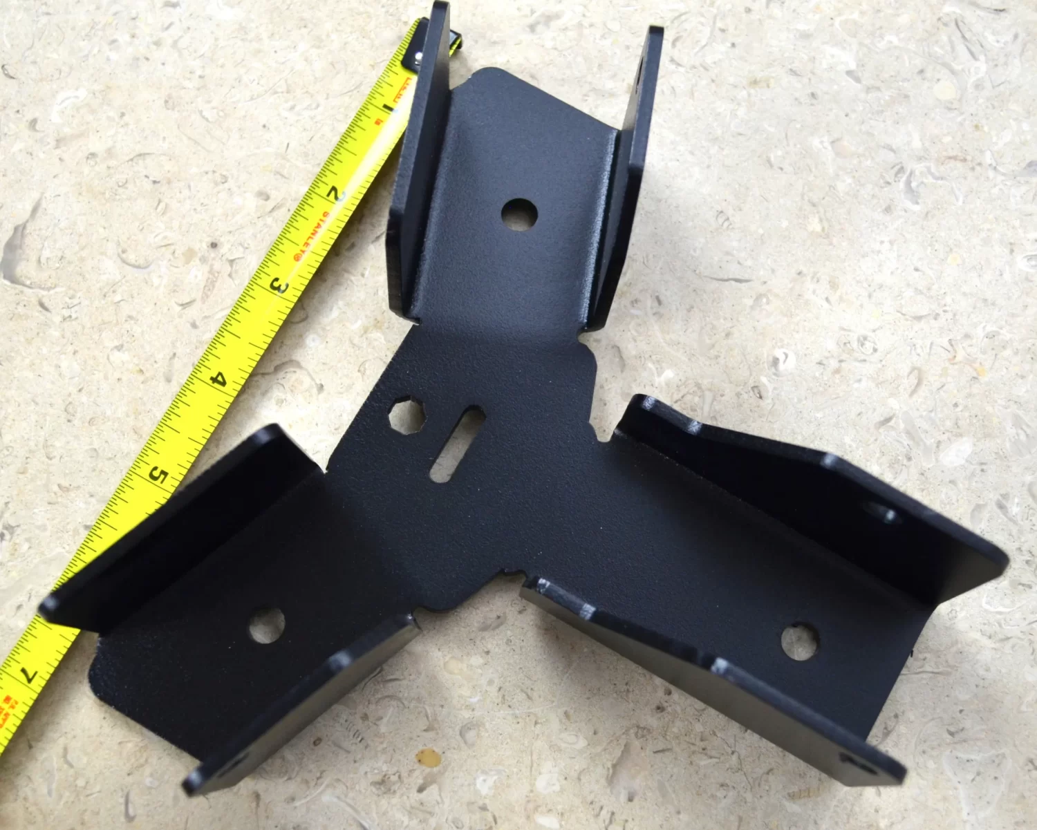 DSC_0097 Heavy Duty Octagon CrossTie Bracket featuring multiple angled flanges and holes, shown on a light-colored stone surface beside a yellow measuring tape.