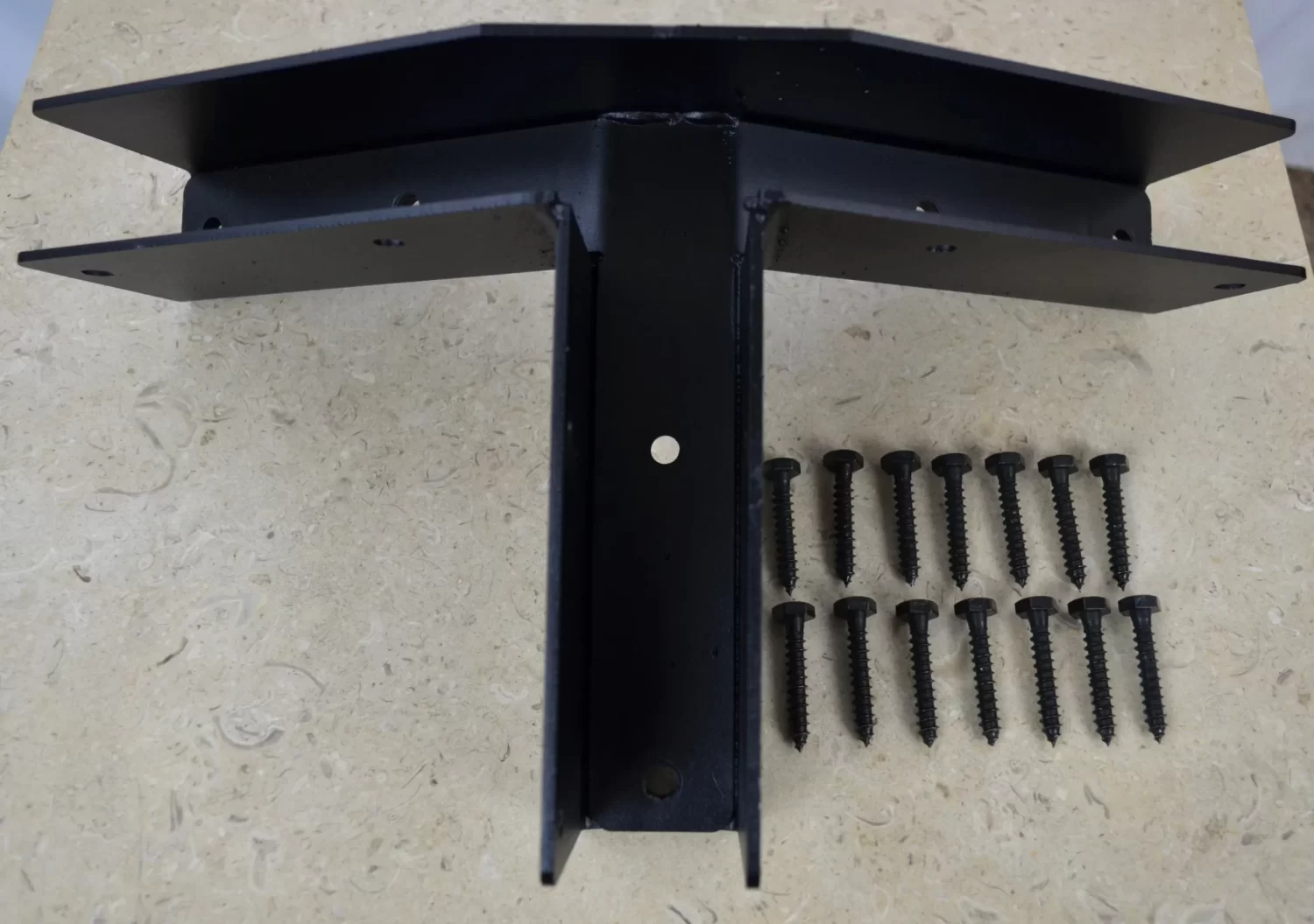 DSC_0023 5-12 Pitch Gable End Truss Rafter Bracket made of black metal with a central hole, displayed on a beige surface. Twelve black screws are neatly arranged in three rows to the right of the bracket.