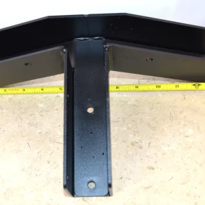 DSC_0073 The 5-12 Pitch Gable End Truss Rafter Bracket, made of black metal with three T-shaped arms, is shown on a light wooden surface with a yellow measuring tape behind it to indicate its width.