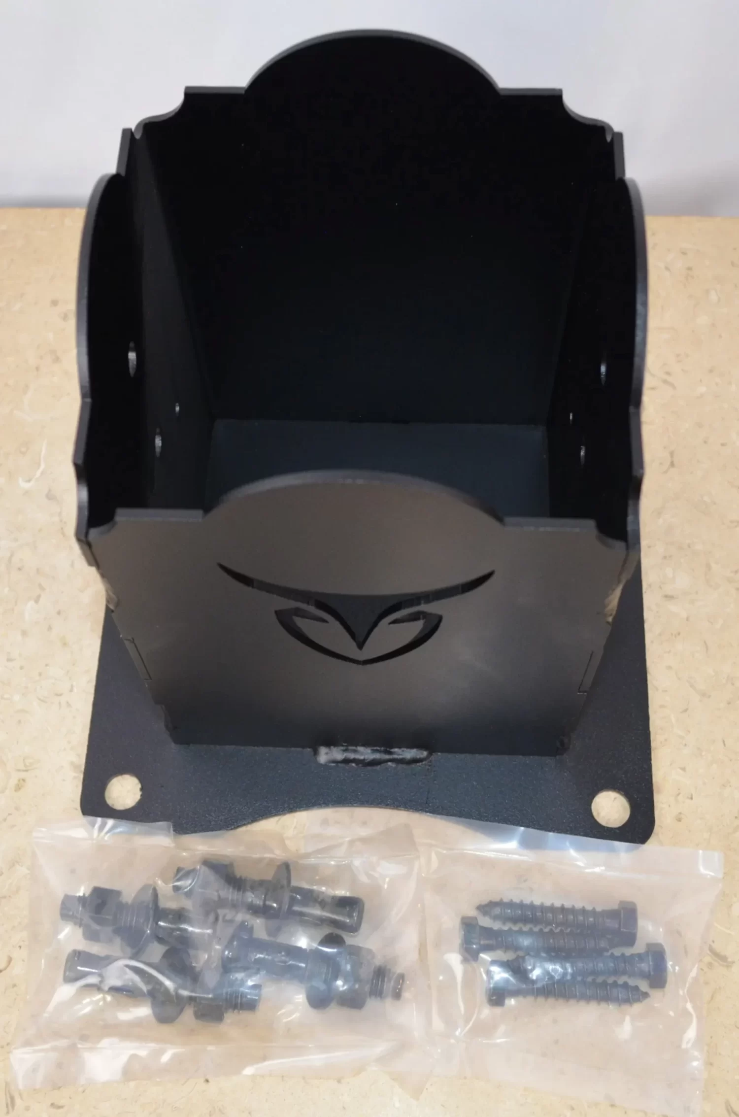 A stylish wooden post holder is sitting on a table, displaying a distinct design at its base. Laying in front of this bracket are bags with 4 concrete anchors and 4 lag screws.