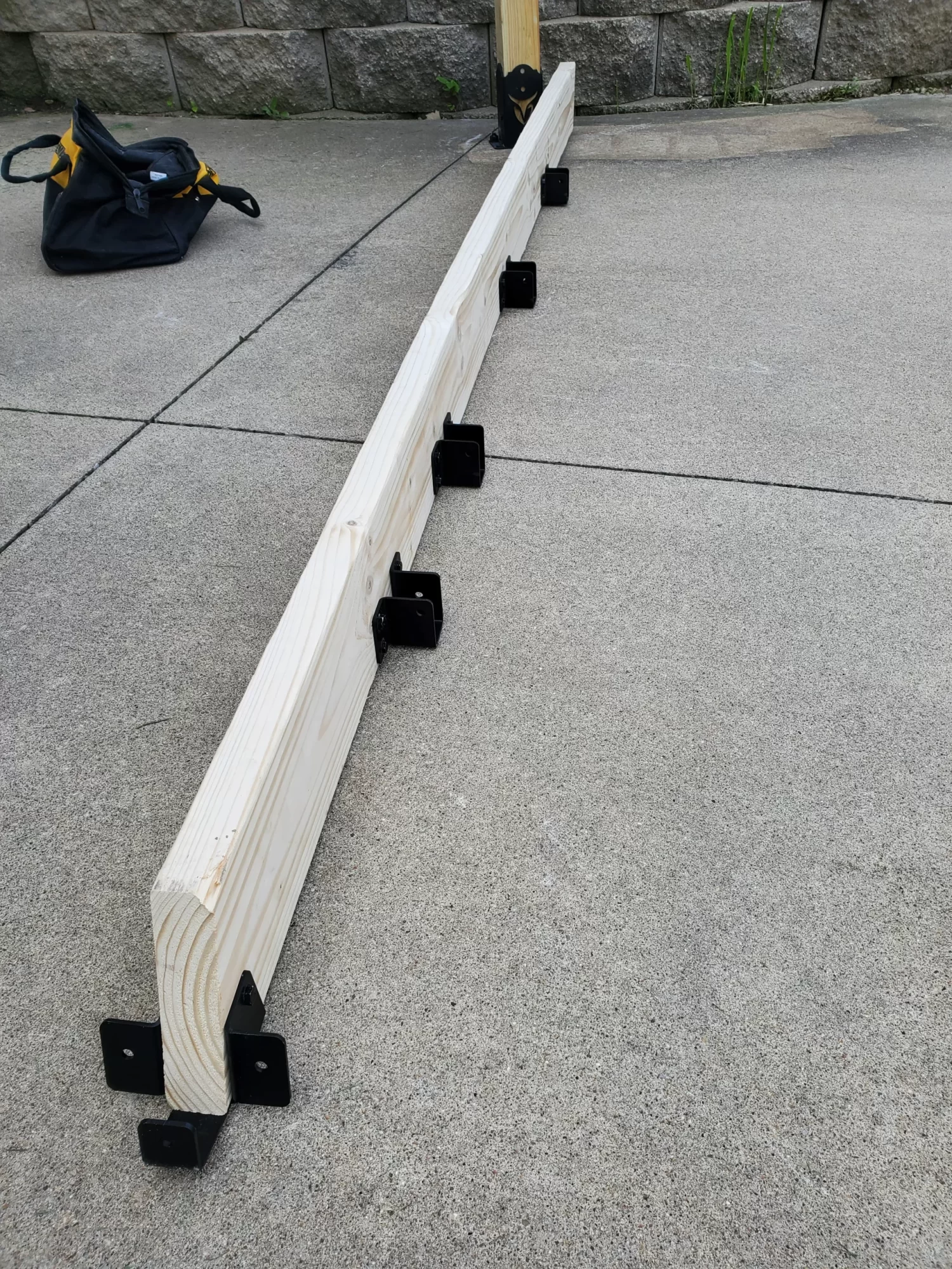 a wooden plank secured with metal brackets rest on a concrete floor in a workshop setting, indicating preparations for a construction project.
