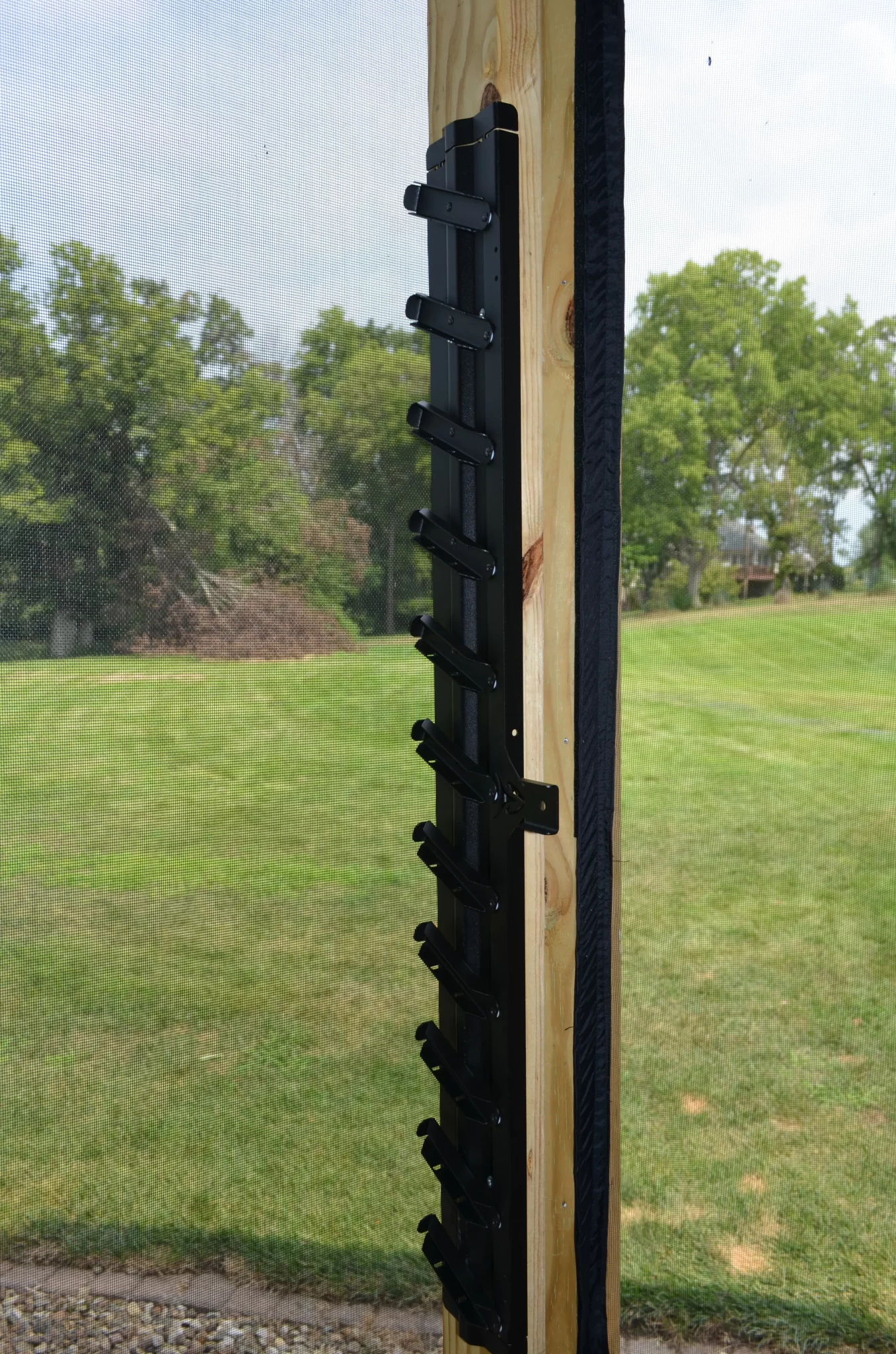 DSC_0072 A Decorative 36 DIY Louver Kit in black metal is mounted vertically on a wooden post outdoors, featuring angled slots with green grass and trees visible in the background.