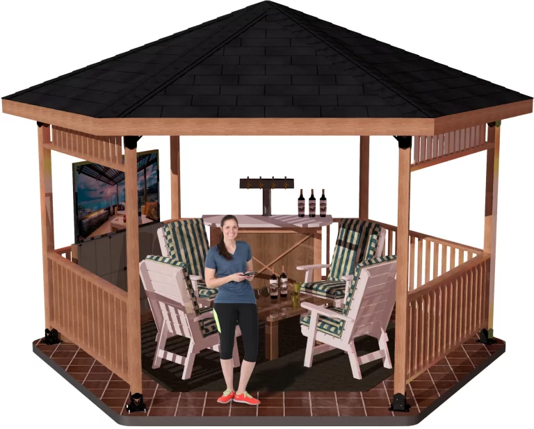 A woman smiles inside a wooden gazebo with a black shingled roof supported by Universal 4x4 Post Anchor Brackets, furnished with cushioned chairs, a round table, drinks, and a wall-mounted TV. Tiled floor and lighting enhance the inviting space.
