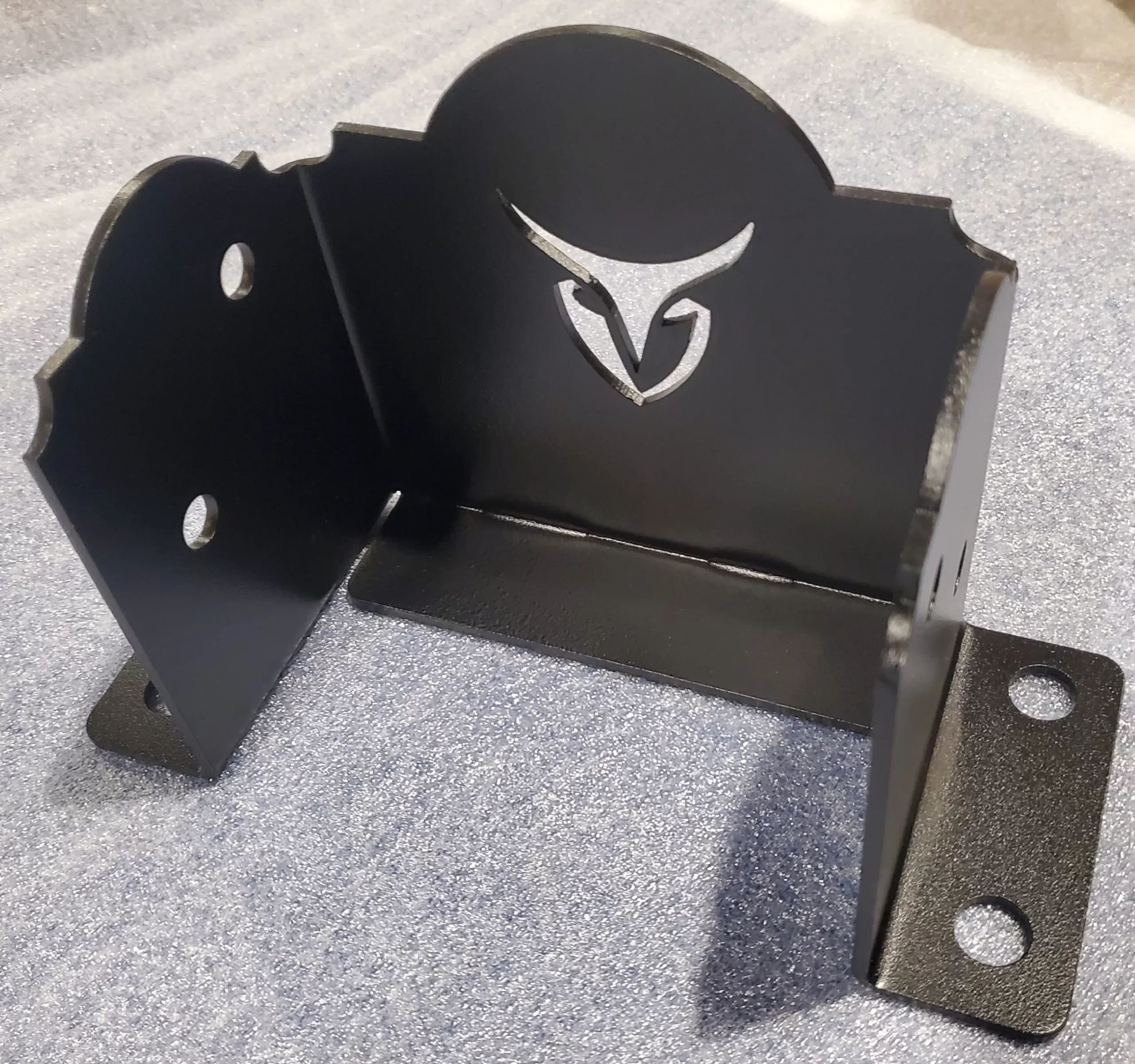 20251117_181051 A black metal bracket with ornate cutouts and a stylized owl face design on one side, placed on a textured gray surface. The bracket has mounting holes and sturdy construction.